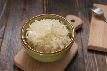 Sauerkraut in a plate on a wooden background.