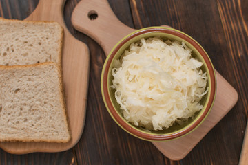 Sauerkraut in a plate and a piece of bread on a wooden background.