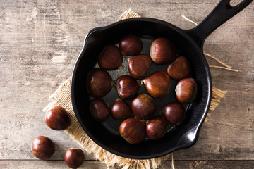 Chestnuts in iron pan on wooden table. Top view