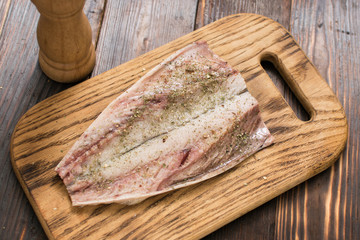 Fresh mackerel fish fillet sprinkled with spices on a wooden background. Preparation of fish for cooking.