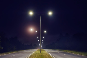 a two way road is illuminated by the light post - obrazy, fototapety, plakaty