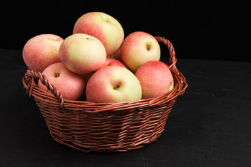Ripe raw apples in wicker basket on black background with copy space - organic yellow and red fruits.