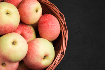 Ripe raw apples in wicker basket on black background with copy space - organic yellow and red fruits.