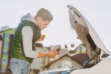 side view of young man checking engine oil level in broken car