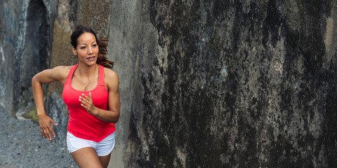 Female fit hispanic athlete running against concrete wall in background for copy space. Sporty fitness cheerful woman training.