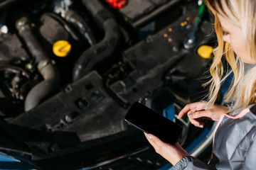 Plakat cropped shot of girl using smartphone with blank screen while fixing broken car