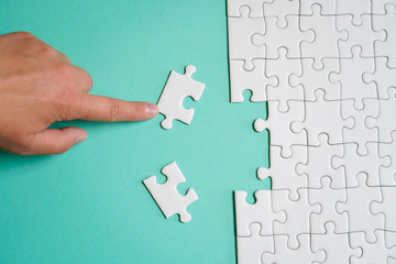 Fragment of a folded white jigsaw puzzle and a pile of uncombed puzzle elements against the background of a colored surface.