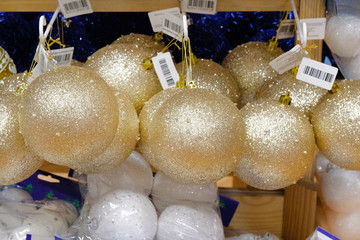 Christmas sparkling balls sold in store. Gold bright glass balls on shelves of large shop. Close up.