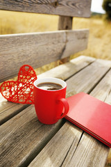Red mug with coffee in a wooden bench outdoors in the morning