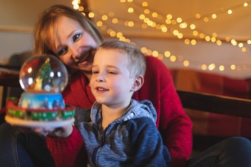 Mother and son holding Christmas tree snow globe at home