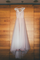 Fototapeta na wymiar Close up of wedding dress in pastel rose hangs, wooden background