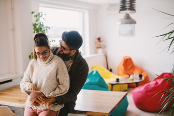 Couple looking at tablet while leaning on the table. Home interior.