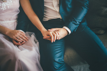Elegant groom and bride sitting. holding their hands, close up