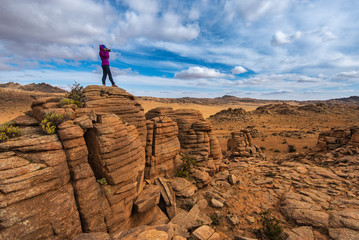 girl takes pictures fantastic view at rock formations and stacked stones on granite hilltops. Baga...