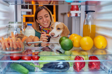 Woman feeding dog while standing in front of fridge full of groceries. Picture taken from the inside of fridge.