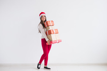 Christmas and holidays concept - young woman in santa hat holding stack of gift boxes over white background with copy space