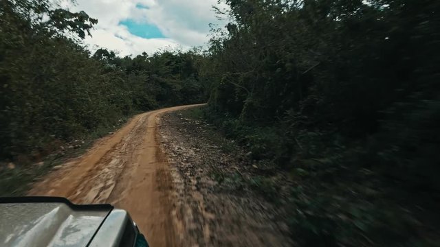 a 4x4 car suv vehicle driving on a remote muddy dirt road across the rainforest