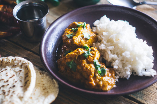 Chicken Tikka Masala (traditional indian curry) with rice and indian bread chapati decorated with spicy red chili peppers, cilantro, Indian spices (turmeric, garam masala) on an old wooden table