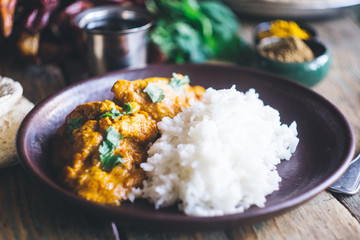 Chicken Tikka Masala (traditional indian curry) with rice and indian bread chapati decorated with spicy red chili peppers, cilantro, Indian spices (turmeric, garam masala) on an old wooden table