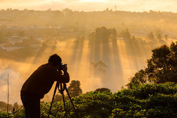 Fototapeta premium Photographer take photos with mirror camera on peak of mountain. misty landscape, spring orange pink misty sunrise in beautiful valley below.
