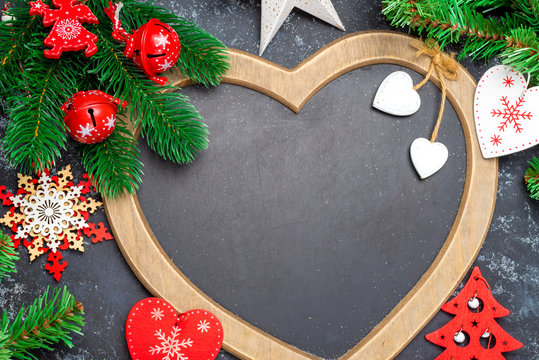 Christmas or New Year decorations background: a frame in the shape of a heart is surrounded by branches of a New Year tree Christmas decorations, toys, on a black background Copy space, top view, flat