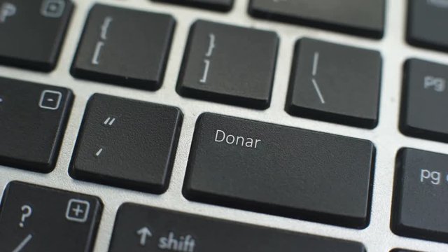 Donate in Spanish button on computer keyboard, female hand fingers press key