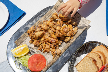 aerial view of hand of child taking fried baby squids on tray