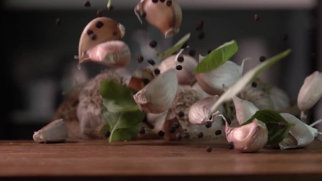 Garlic falling with pepper and leaves to wood cutting board, on kitchen background. Slow motion 480 fps. Sony rx 10