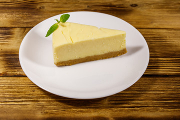 Piece of tasty sweet New York cheesecake in a white plate on wooden table