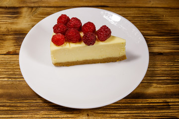 Piece of tasty New York cheesecake with raspberries in a white plate on wooden table
