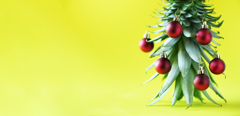 Creative Christmas tree made of pineapple and red bauble on yellow background, copy space. Greeting...