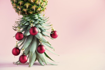 Creative Christmas tree made of pineapple and red bauble on pink background, copy space. Greeting card, decoration for new year party. Holiday concept.