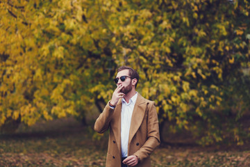 stylish man in an autumn coat smoking a cigarette in the park