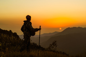 girl traveler with a camera case and trekking poles walks through the mountain pass and looks at the setting sun