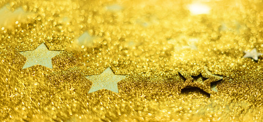 Golden glitter stars on yellow background. Gold shiny texture, copy space for your Christmas greetings. Concept of New year, luxury holiday.