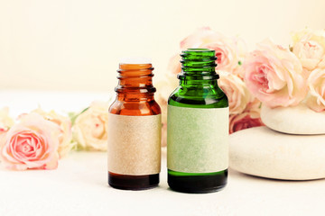 Fototapeta na wymiar Glass bottles of essential oils on table with delicate beige rose flowers, spa stones. Aromatherapy & wellness