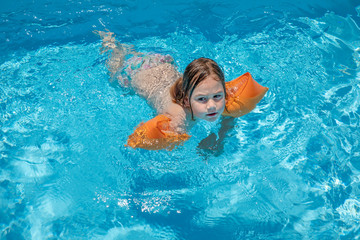 child with armbands swimming in transparent blue water of pool