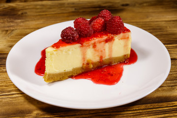 Piece of tasty New York cheesecake with raspberries and raspberry jam in a white plate on wooden table