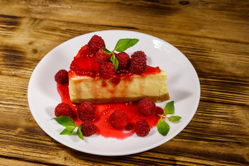 Piece of tasty New York cheesecake with raspberries and raspberry jam in a white plate on wooden table