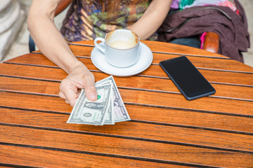 Fototapeta na wymiar detail of woman hand with dollar bills coffee cup and mobile phone on table
