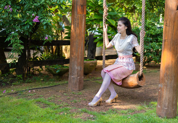 happy woman in Thai traditional dress relaxing on a wooden swing
