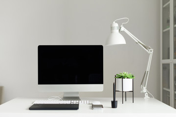 Modern white office desk table, mockup desktop computer, lamp, graphics tablet, keyboard, mouse, pen, succulent plant. Copy space. Scandinavian home, minimalistic style.