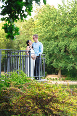 Asian pregnant women and caucasian husband standing near iron railings in park
