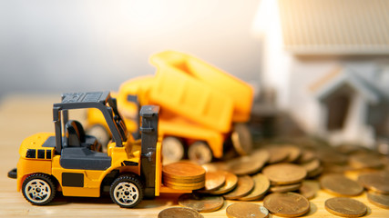 House and construction truck models with gold coins spilling on wooden table. Real estate...