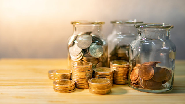 Coins in currency glass jars and stack on wooden table. Saving money for future retirement. Financial business investment concept
