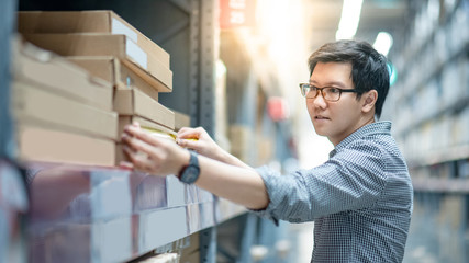 Asian man worker using tape measure for measuring cardboard box product in warehouse.