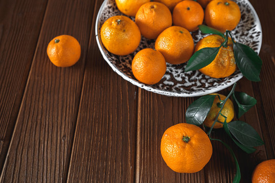Fresh delicious mandarin oranges fruit or tangerines with green leaves in a bowl on wooden background
