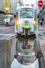Tuc Tuc reflection in a puddle in Lisbon with another Tuc Tuc coming on the street