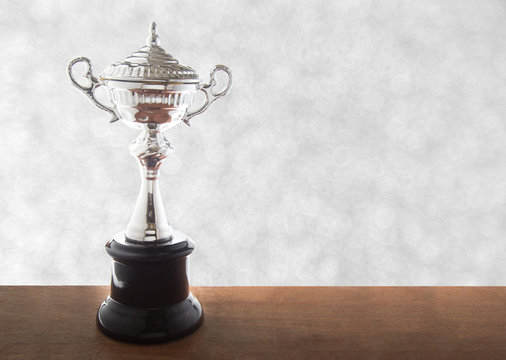 Silver trophy on wooden table over abstact white bokeh background. Winning awards with copy space.