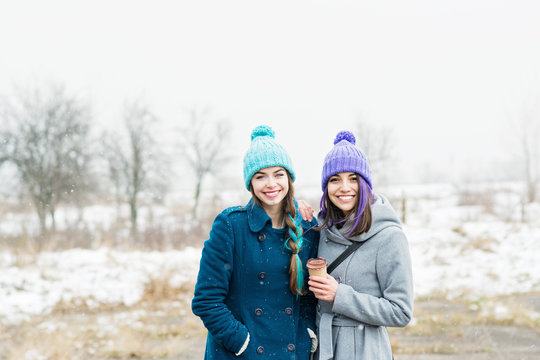 Two female friends outdoors in winter on snowy day, smiling and posing together. No retouch, natural lighting.